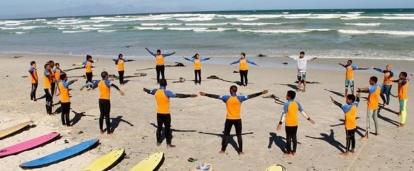 A group of children stretching during volunteer surf coaching in South Africa. Projects Abroad volunteers teach surfing in South Africa through warm up exercises.